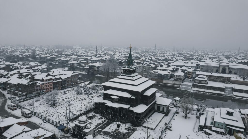 Aerial view of snow-covered Srinagar city, showcasing a traditional mosque in winter scenery.
